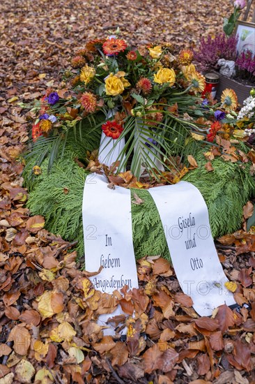 Flower wreath with mourning bows on autumn leaves at a memorial tree with the names of those buried there in Seelwald