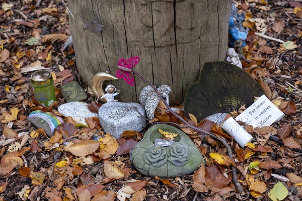 Mementos and stones in the shape of a heart on a memorial tree with the names of the buried