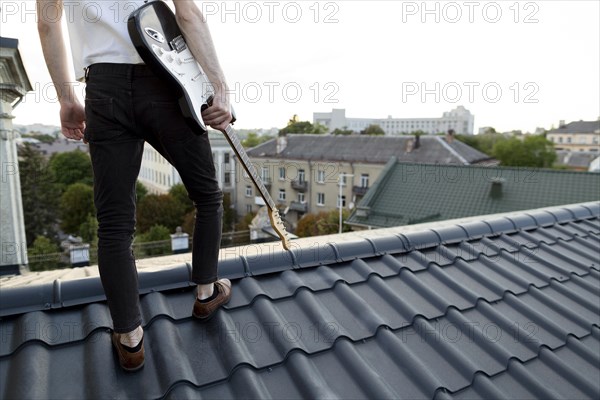 Back view male musician roof top holding electric guitar