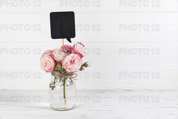 Black speech bubble prop rose glass jar against white wooden backdrop