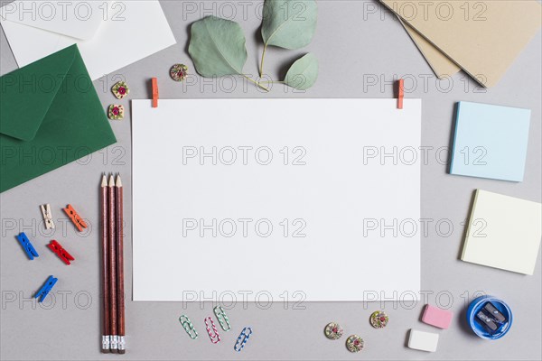 Blank white page with clothes peg surrounded with stationeries gray background