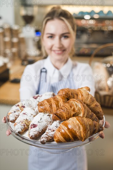 Blurred young woman offering croissants glass cake stand