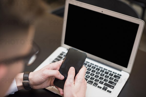 Businessman s hand using mobile phone front laptop