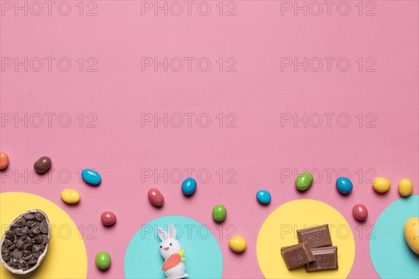 Choco chips rabbit statue chocolate pieces colorful candies pink backdrop with space text