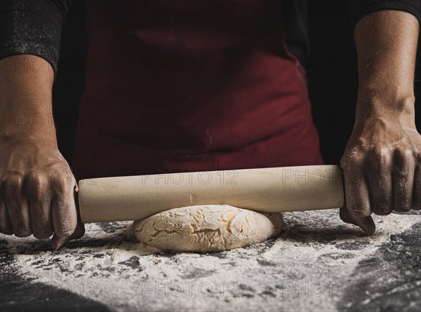 Close up baker rolling dough composition