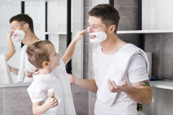 Close up boy applying shaving foam his father s face bathroom