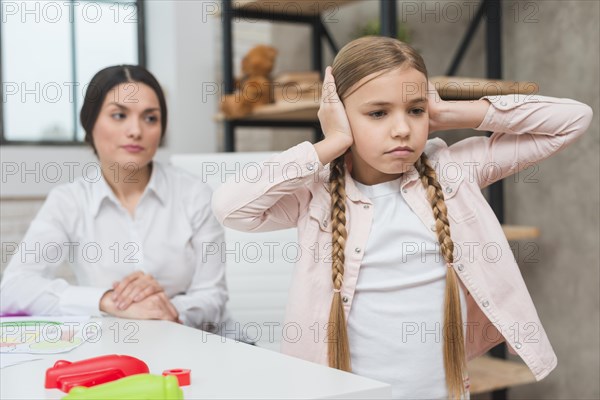 Close up female psychologist looking annoyed girl covering her ears with two hands