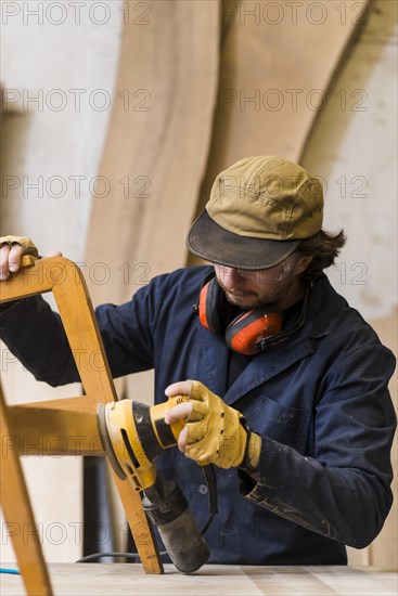 Close up male carpenter sanding furniture with power tool workbench