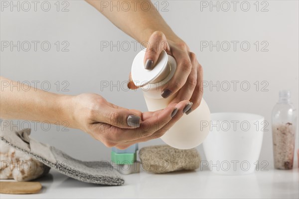 Close up woman s hand pouring sanitizer soap from dispenser with spa product white desk against background