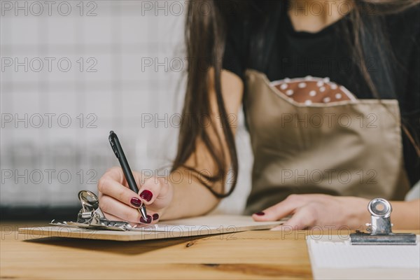 Crop waitress writing clipboard