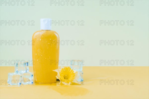 Crystal ice cubes with daffodil flower yellow sunscreen lotion bottle against green backdrop