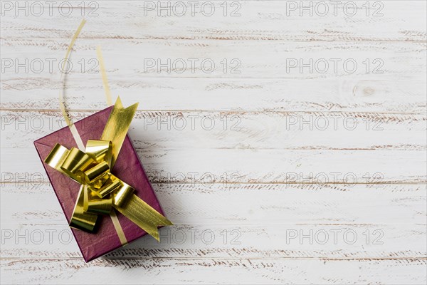 Decorated gift box with golden ribbon textured white wooden surface