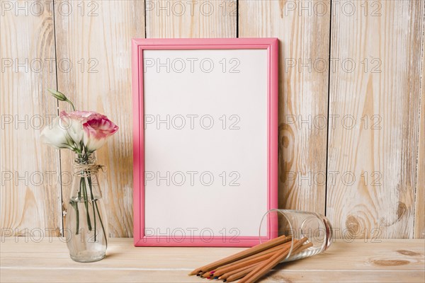 Eustoma glass vase colored pencils white picture frame with pink border wooden table