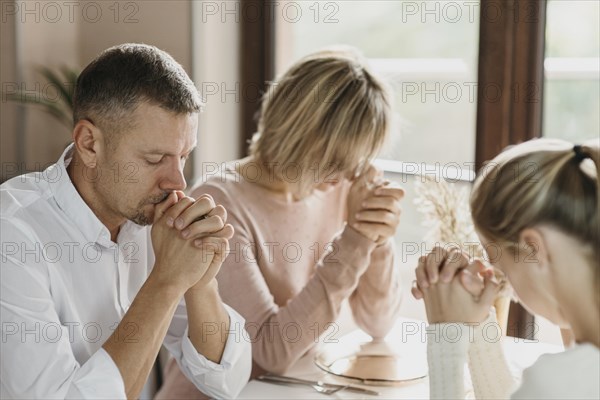 Family praying together before eating indoors