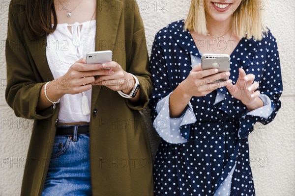 Female friends leaning wall using smartphone