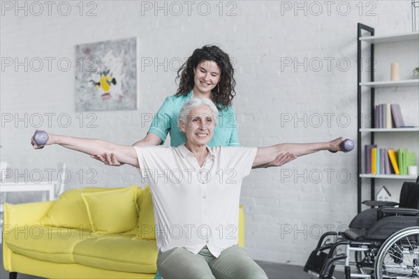 Female nurse assisting senior woman exercise with dumbbells