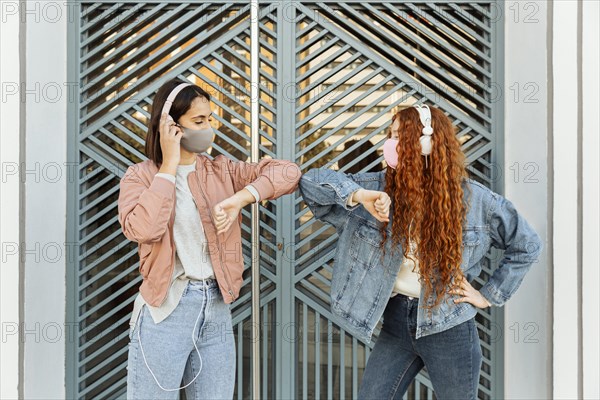 Front view female friends with face masks outdoors doing elbow salute