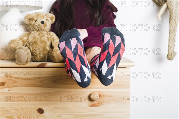 Girl sitting near soft toy showing her feet with multi colored socks
