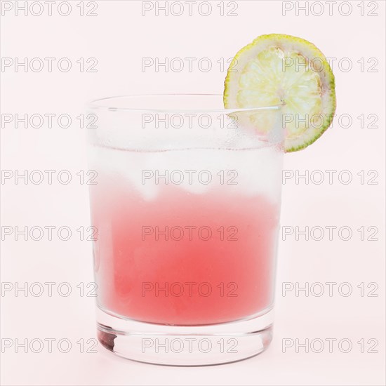 Glass cocktail drink with lemon slice against pink background