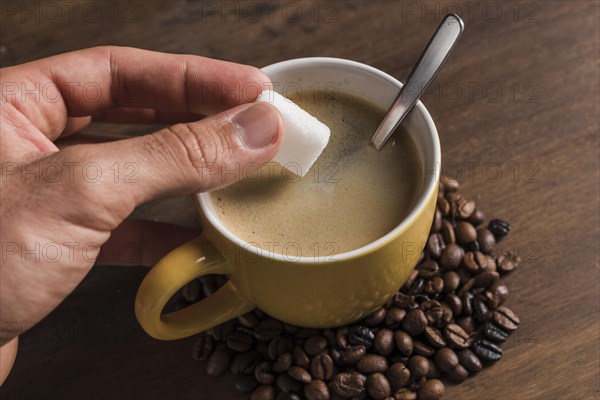 Hand holding sugar near cup with coffee