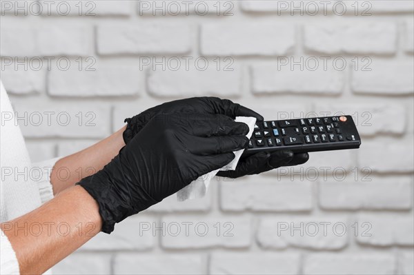Hands with gloves disinfecting remote control