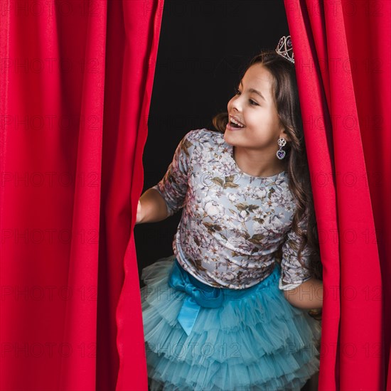 Happy girl peeking from red curtain stage