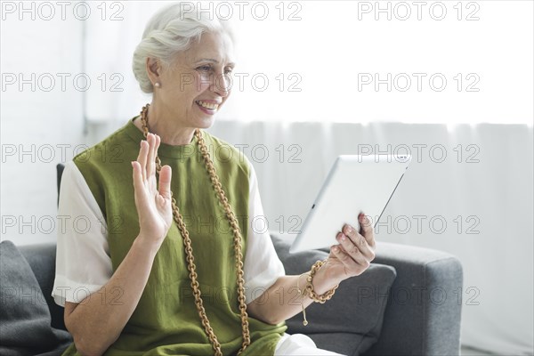Happy woman sitting sofa saying goodbye digital tablet