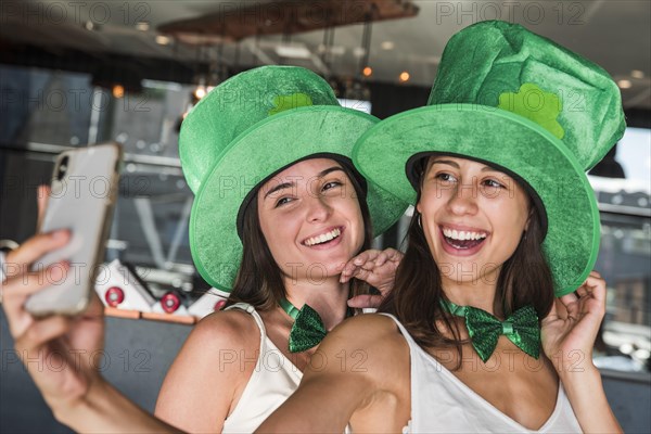 Happy young women saint patricks hats taking selfie smartphone