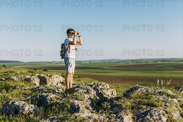 Hiker standing rock looking through binocular