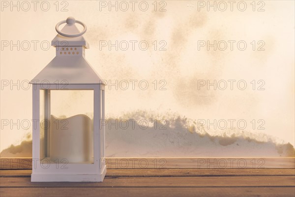 Lantern with candle wood board near heap snow through window