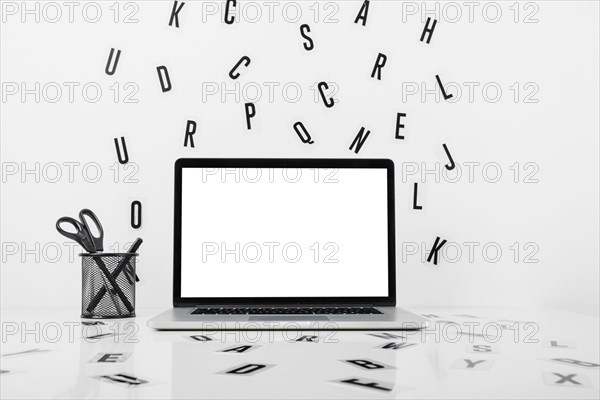 Laptop with blank white screen near pencil holder alphabets white surface