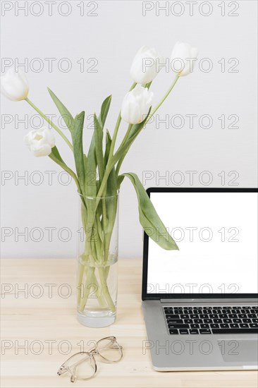 Laptop with white tulips vase table