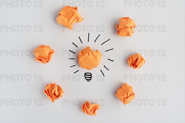 Light bulb with crumpled colorful paper white surface