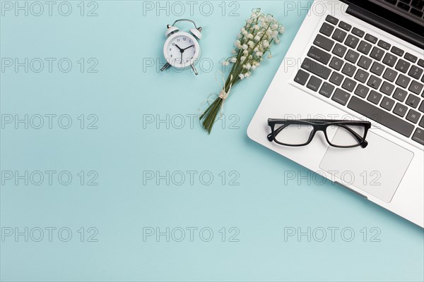 Lily valley bouquet with alarm clock eyeglasses laptop blue office desk
