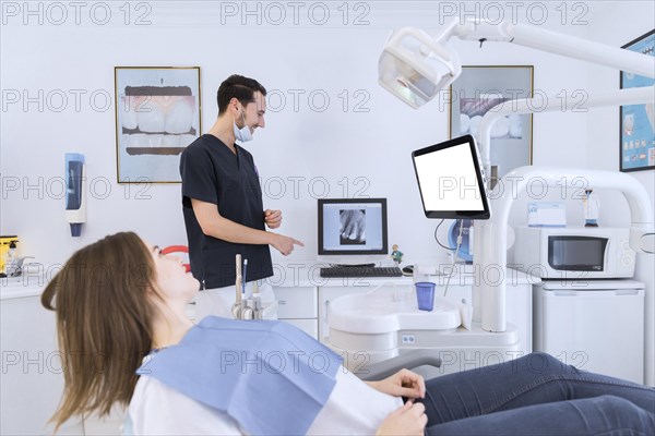 Male dentist explaining teeth x ray screen female patient lying dentist chair