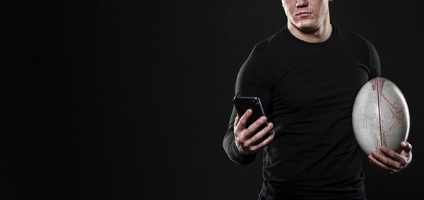 Male rugby player using smartphone while holding ball with copy space