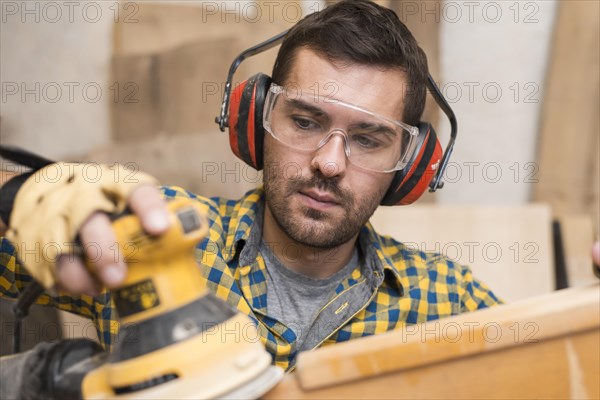 Man builder carpenter polishes wooden board with random orbit sander