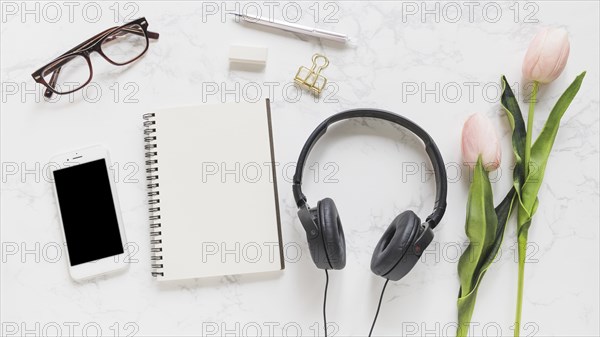 Mobile phone eyeglasses notebook stationery headphone pink tulips marble backdrop