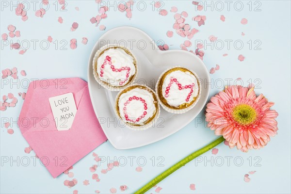 Muffins with mom word plate near flower envelope with tag confetti