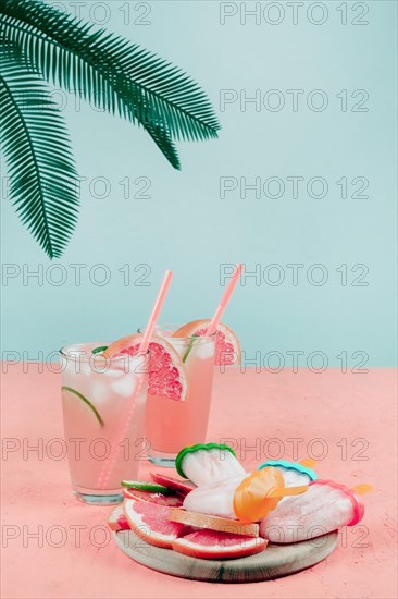 Palm leaves grapefruit cocktail glasses popsicles coral desk against teal background