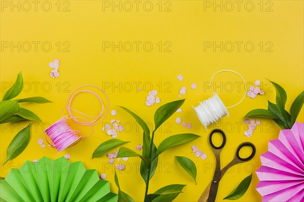 Paper flower confetti green leaves thread spool yellow background
