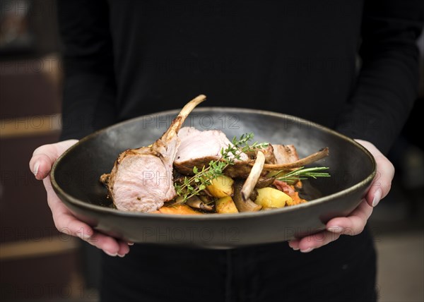 Person holding lamb ribs dish