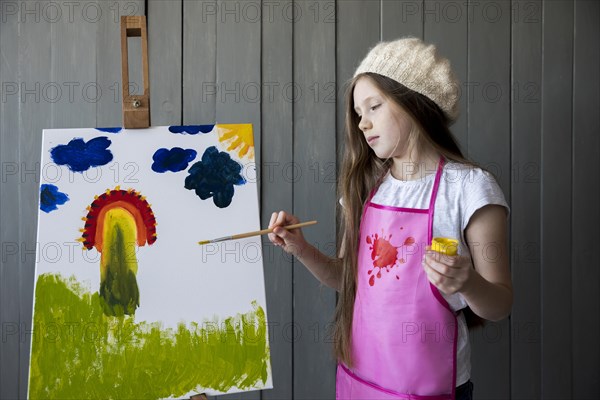 Portrait cute girl painting easel with paintbrush
