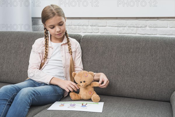 Portrait girl showing family drawing paper her teddy bear