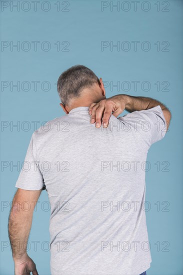 Rear view man suffering from neck pain front blue backdrop