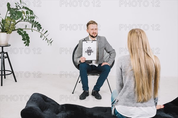 Serious male psychologist showing paper with rorschach inkblot female patient