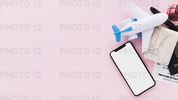 Smart phone with blank screen display with travel passport map tickets toy airplane sunglasses pink background