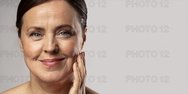 Smiley elder woman with make up posing with hand face copy space