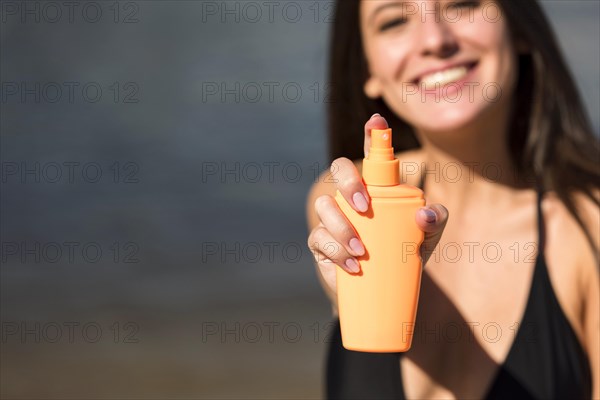 Smiley woman holding sunscreen beach with copy space