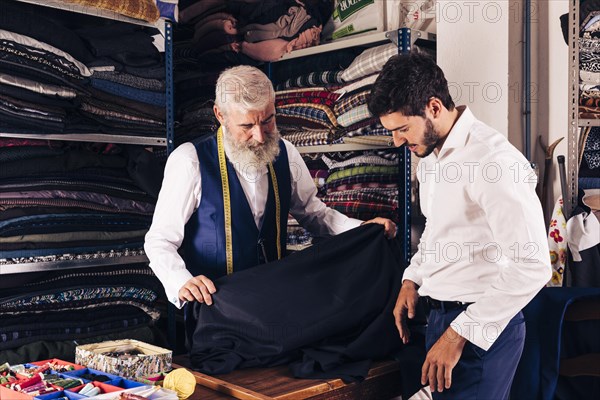 Smiling man seller displaying blue fabrics young customer textile shop